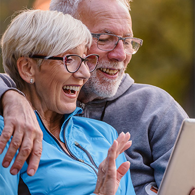 Two seniors outside on a park bench looking happily at a tablet together.